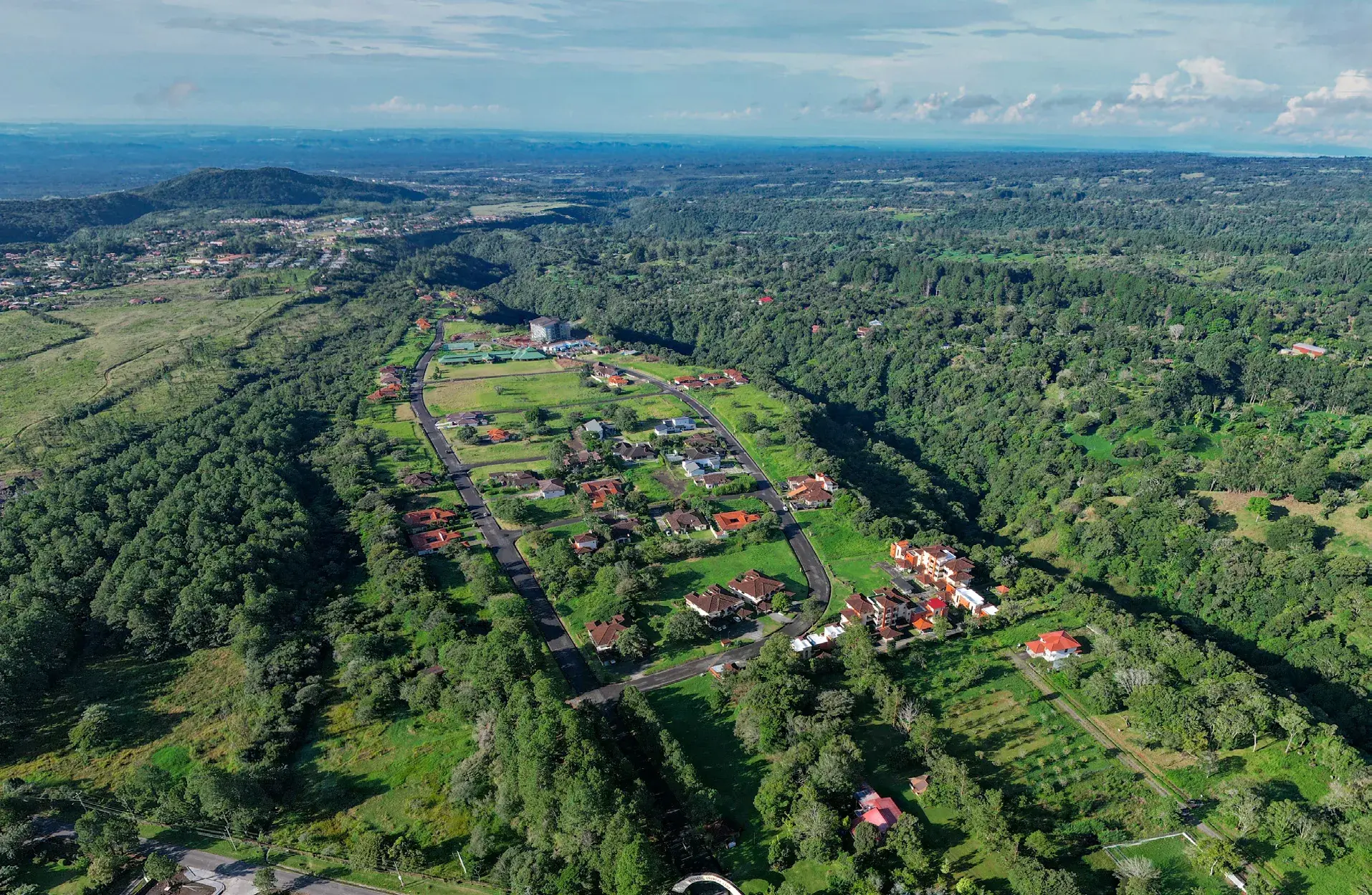 Aerial photo of the Boquete Country Club community, with a looping road, scattered tile-roofed homes, a condo building and open lots in forested hills.