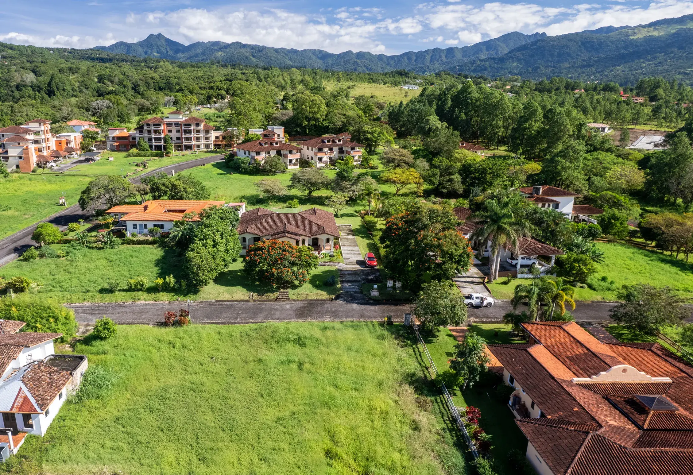 Aerial photo of tile-roofed homes, condo buildings and open green lots at Boquete Country Club, with mountains behind.