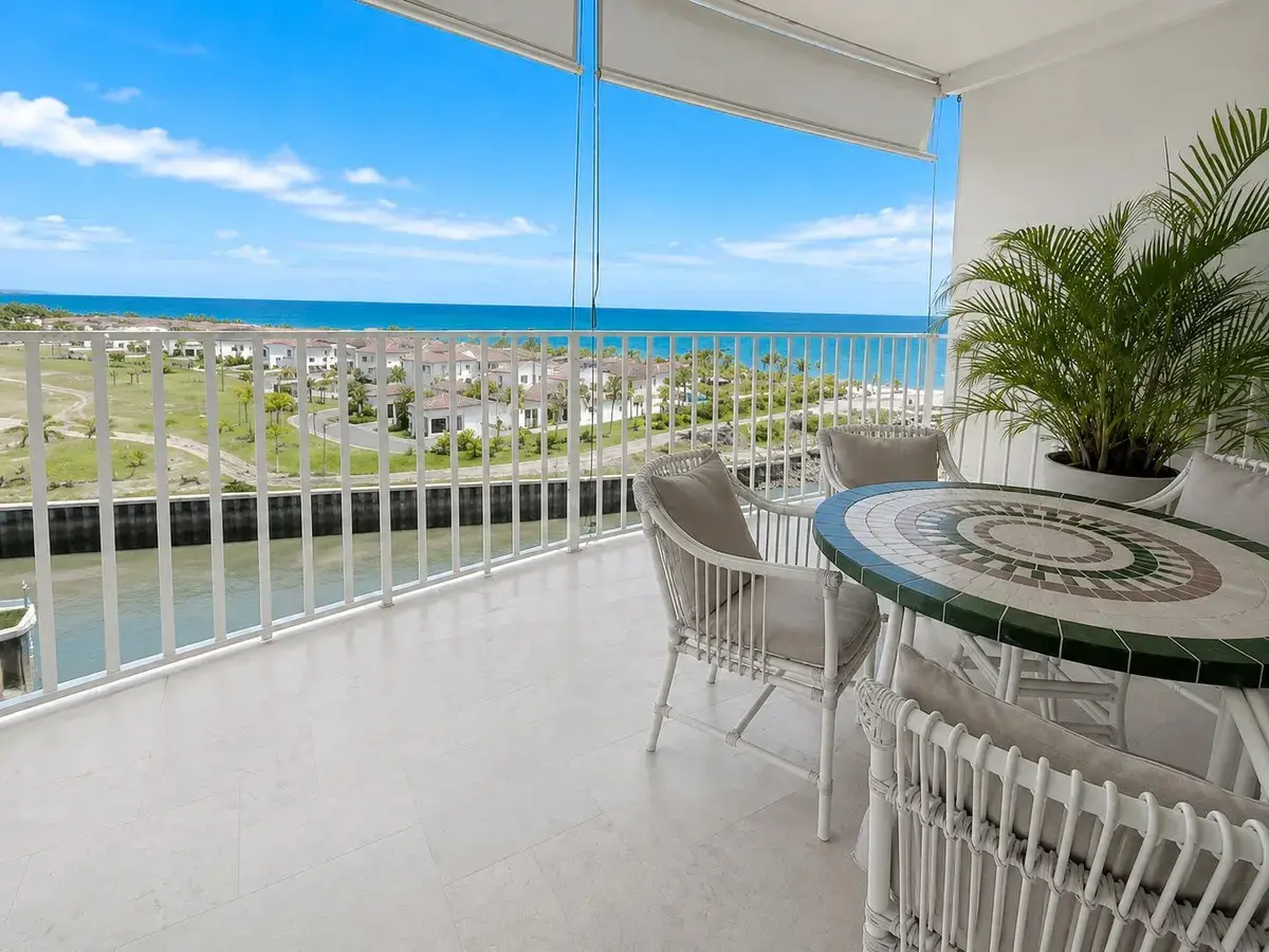 Balcón en Puntarena Ocean Village con mesa de mosaico y sillas de mimbre blancas, con vista al canal de la marina, casas de techo rojo y el Pacífico.