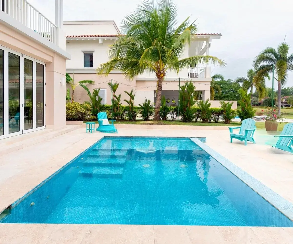 Private pool at Ocean Lakes villa 7 with turquoise Adirondack chairs on a cream stone deck, palms and the neighboring villa behind.