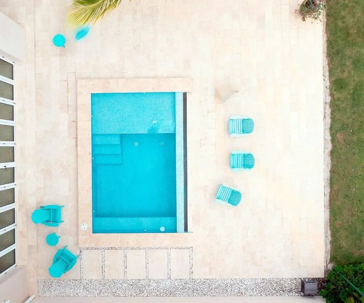 Overhead view of the pool and stone deck at Ocean Lakes villa 7 with four turquoise chairs beside the lawn.