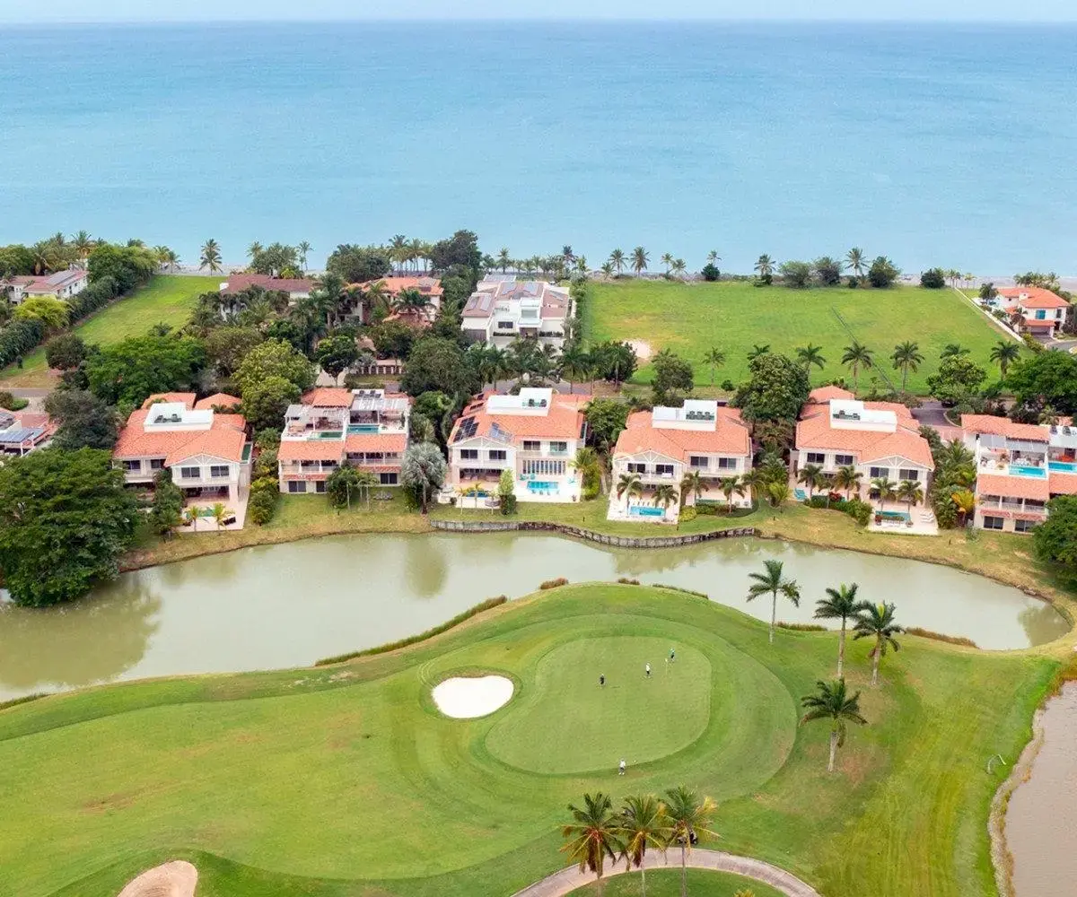 Aerial view of a row of two-level villas with tile roofs at Ocean Lakes, Buenaventura, between a lake with a golf green and a lawn running to the sea.